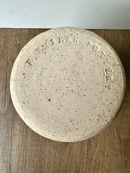 The unglazed bottom of the white ceramic vessel with black speckles; "K. Embers Pottery" stamped in.