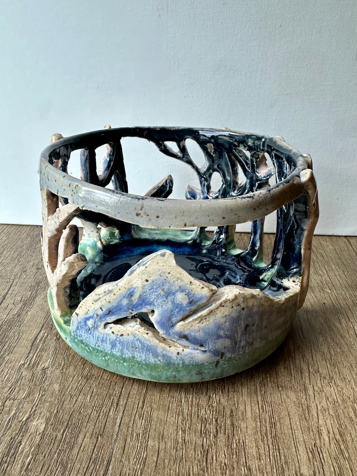 Round ceramic candle surround with mountain and birch trees cut out.