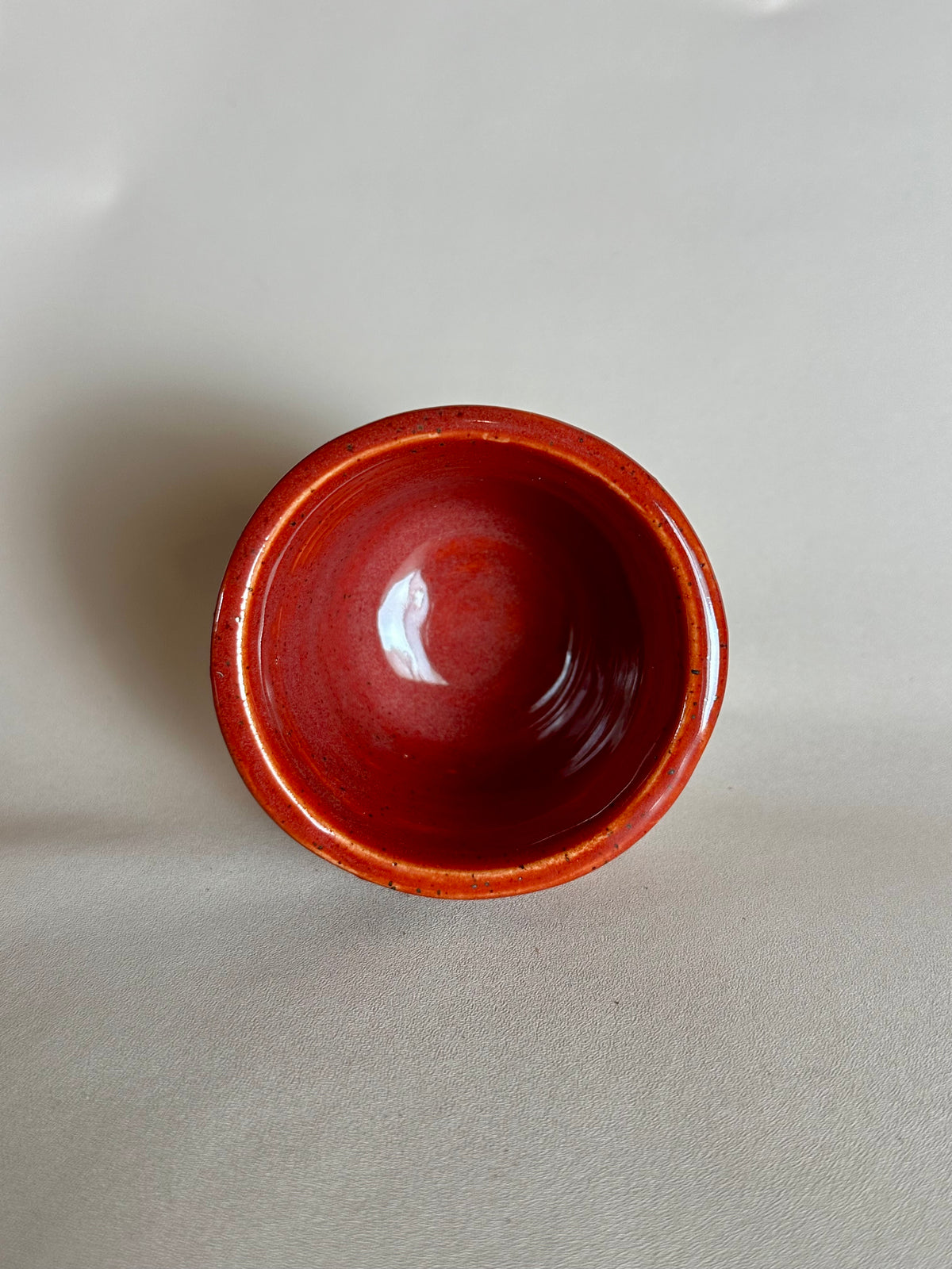 A small handmade ceramic cup with a glossy deep red glaze, photographed from directly above on a neutral light gray background.