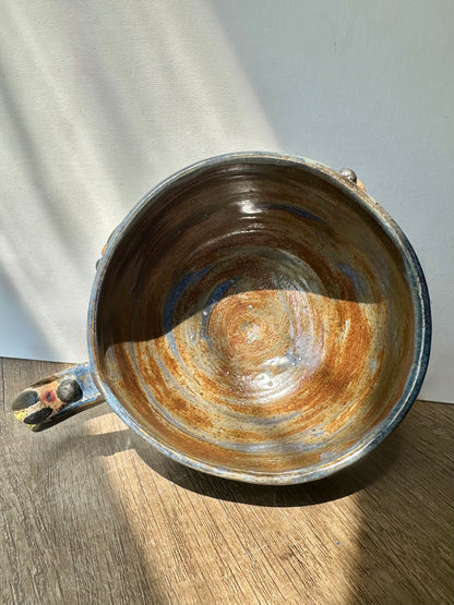 Interior of mug; bronze-colored with streaks of inky blue and sculpted firefly on the handle.