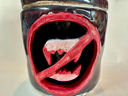 Close up of a glossy black canister with a cut out of a set of bloody vampire fangs inside a red circle with a slash. Set against a solid neutral background.