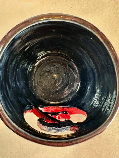 Overhead interior view of a glossy black canister with a cut out of a set of vampire fangs inside a red circle with a slash. Set against a solid neutral background.