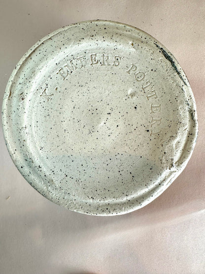 A black-speckled white clay bottom of a ceramic canister that has "K. Embers Pottery" stamped in the base.