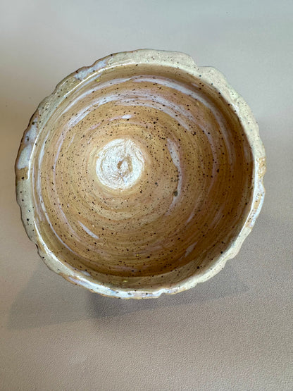 The inside of a small-medium bowl colored to look like a waffle cone bowl; slight glossy white glaze swirls on the inside makes the illusion of melted vanilla ice cream. Photographed from a top-down perspective on a solid neutral beige background.